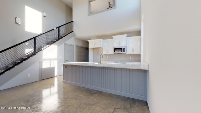 kitchen featuring tasteful backsplash, white cabinets, a towering ceiling, and sink