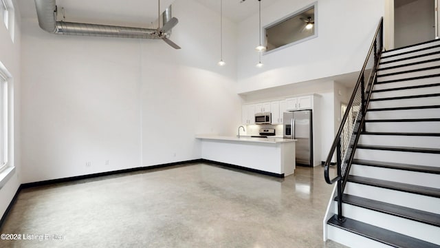 unfurnished living room featuring ceiling fan, sink, and a towering ceiling