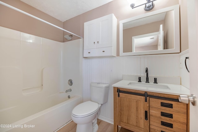 full bathroom featuring toilet, a textured ceiling, hardwood / wood-style flooring, vanity, and washtub / shower combination