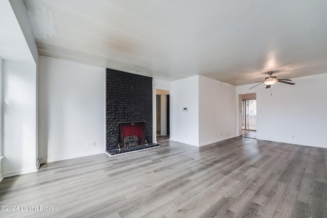 unfurnished living room featuring ceiling fan, a brick fireplace, and light wood-type flooring