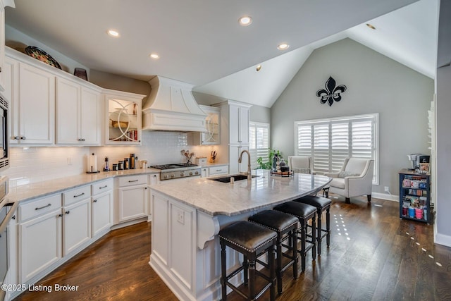 kitchen with sink, premium range hood, a center island with sink, and white cabinetry