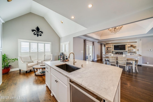 kitchen with stainless steel dishwasher, sink, white cabinetry, light stone countertops, and a kitchen island with sink