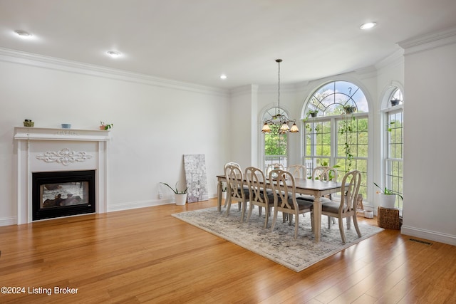 dining area with a multi sided fireplace, wood-type flooring, ornamental molding, and a chandelier