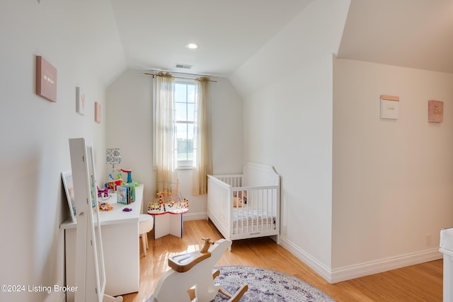 bedroom with light wood-type flooring, lofted ceiling, and a crib