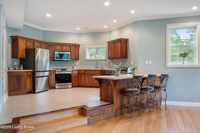 kitchen featuring light hardwood / wood-style floors, kitchen peninsula, ornamental molding, and stainless steel appliances