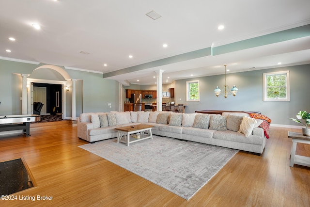 living room featuring light hardwood / wood-style flooring, an inviting chandelier, ornamental molding, and decorative columns