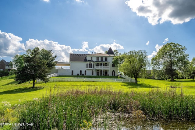 back of property with a balcony, a yard, and a water view