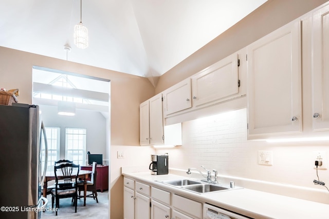 kitchen with pendant lighting, vaulted ceiling, stainless steel fridge, sink, and white cabinetry