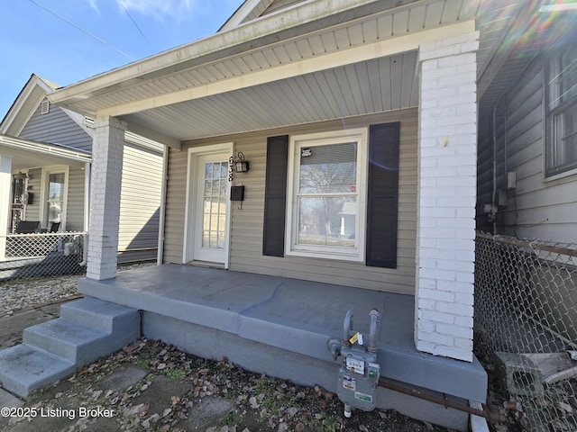 doorway to property with fence, a porch, and brick siding