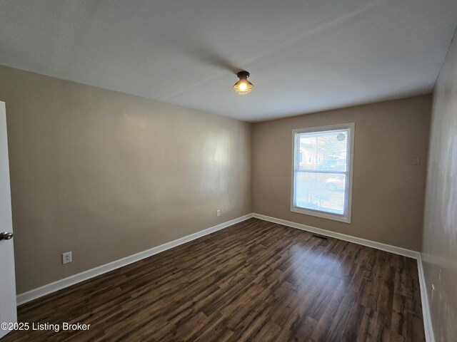 unfurnished room with dark wood-type flooring, visible vents, and baseboards