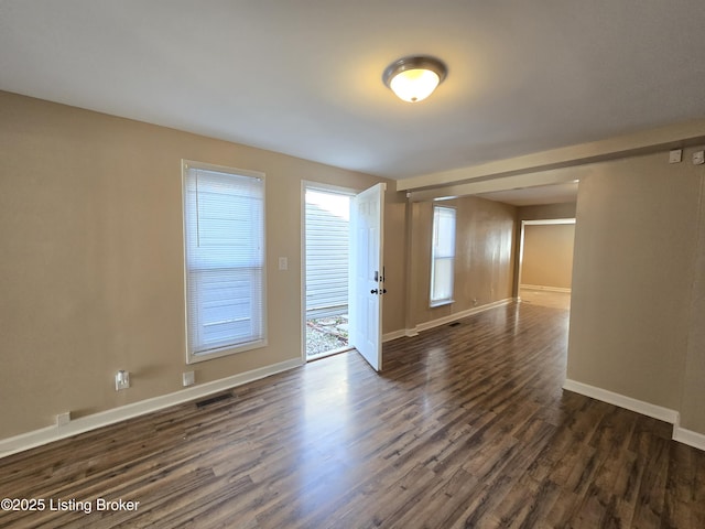 spare room featuring dark wood-type flooring, visible vents, and baseboards