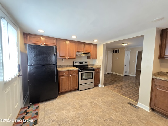 kitchen featuring stainless steel range with electric stovetop, freestanding refrigerator, visible vents, and under cabinet range hood