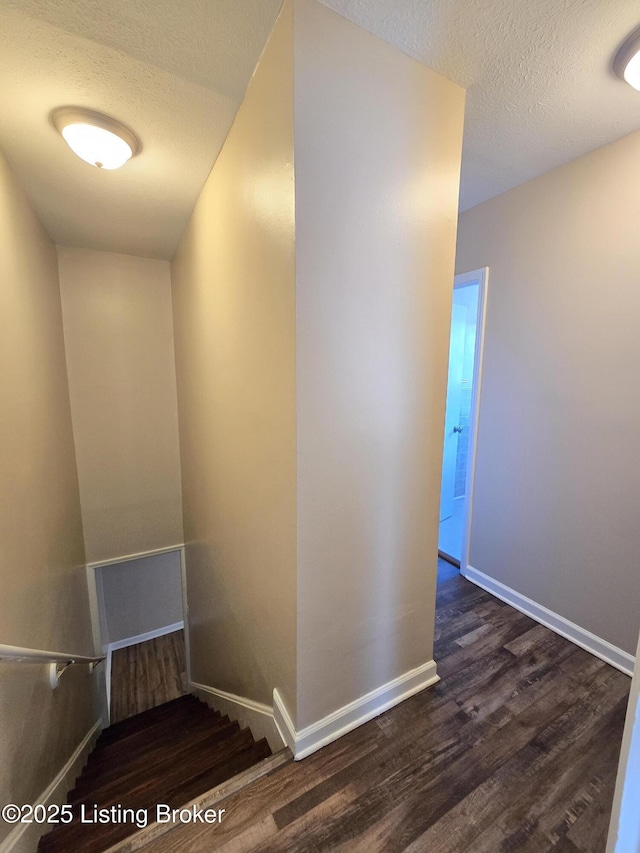 staircase with a textured ceiling, baseboards, and wood finished floors