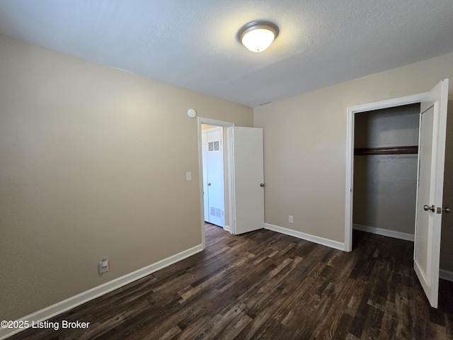 unfurnished bedroom featuring a closet, dark wood-style flooring, a textured ceiling, and baseboards