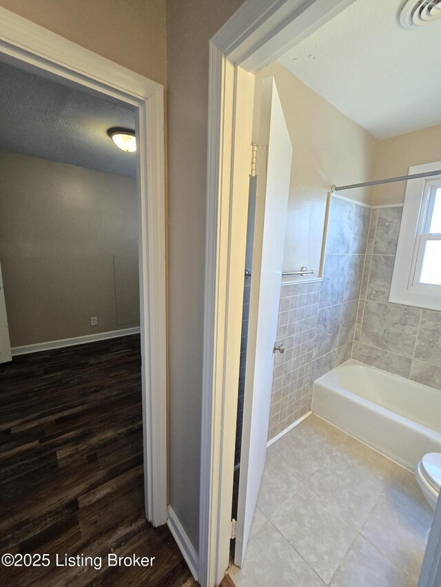 bathroom with tile patterned flooring, toilet, visible vents, baseboards, and washtub / shower combination