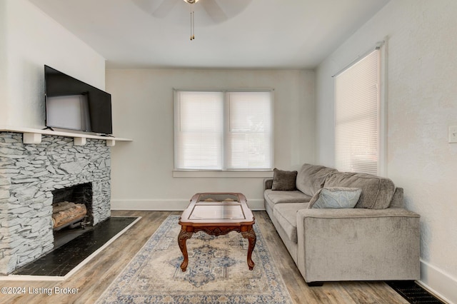 living room with ceiling fan, a stone fireplace, and wood-type flooring