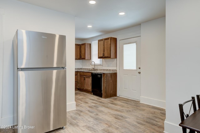 kitchen with black dishwasher, decorative backsplash, sink, light hardwood / wood-style floors, and stainless steel refrigerator