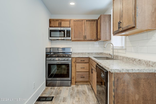 kitchen featuring sink, stainless steel appliances, light wood-type flooring, and backsplash