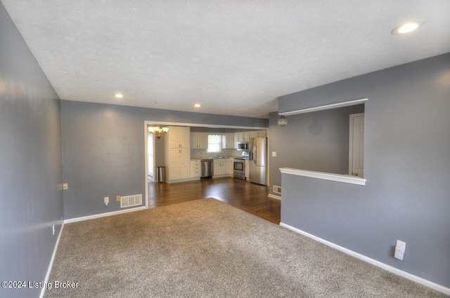 unfurnished living room featuring sink, dark carpet, a textured ceiling, and a chandelier