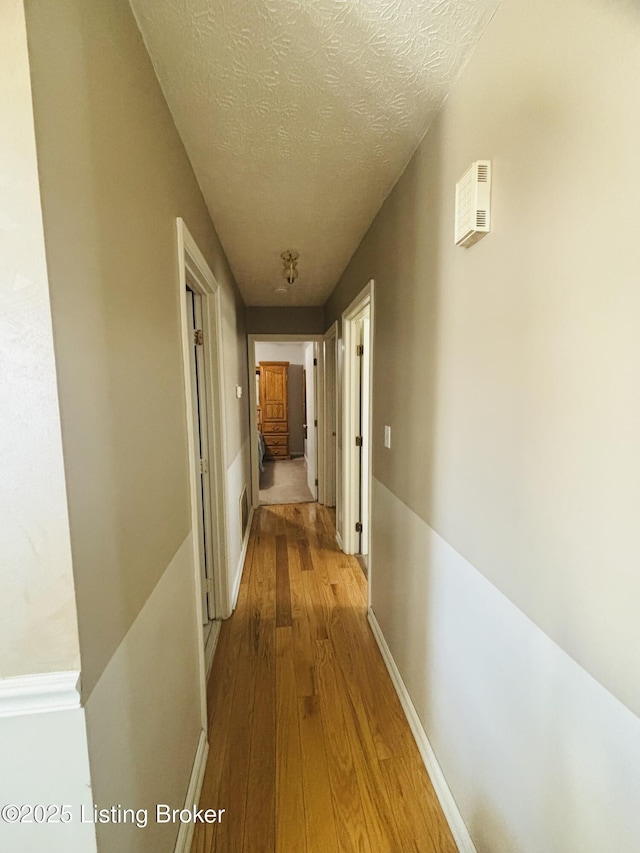 hallway with a textured ceiling and light wood-type flooring