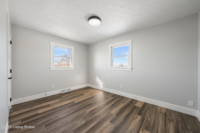 spare room with a healthy amount of sunlight, a textured ceiling, and dark wood-type flooring