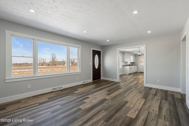 entrance foyer featuring a textured ceiling, dark hardwood / wood-style flooring, a chandelier, and a healthy amount of sunlight