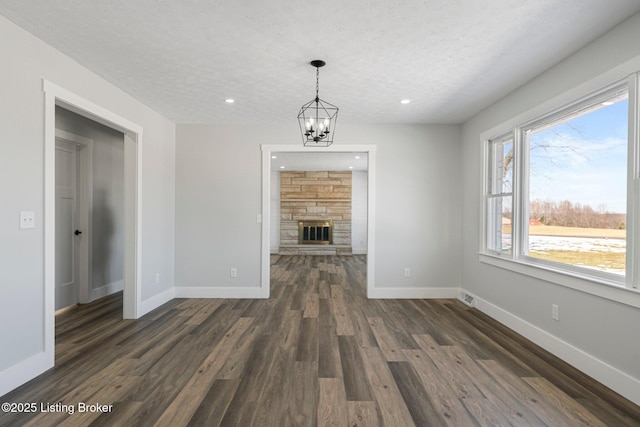 unfurnished living room with a fireplace, a textured ceiling, dark hardwood / wood-style floors, and an inviting chandelier