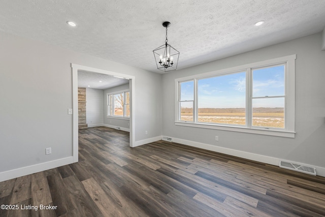 unfurnished dining area with dark wood-type flooring, a textured ceiling, and an inviting chandelier