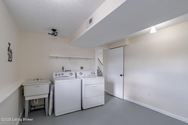 clothes washing area with sink, a textured ceiling, and washing machine and clothes dryer