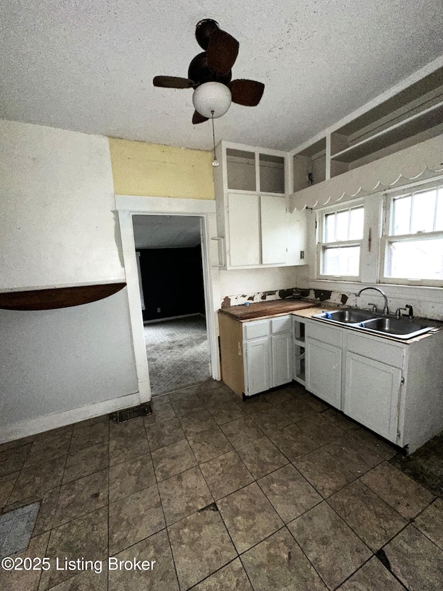 kitchen featuring sink, ceiling fan, white cabinetry, and a textured ceiling