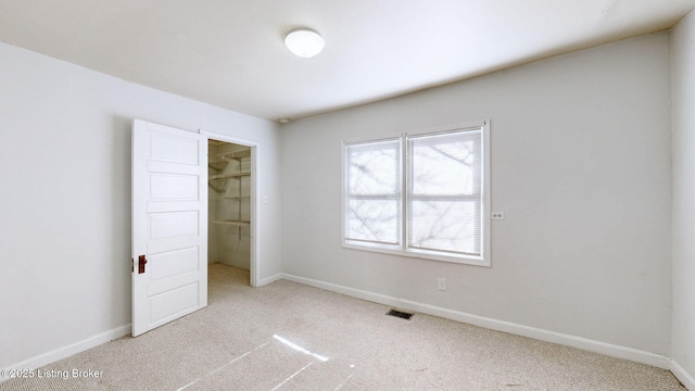 unfurnished bedroom featuring a walk in closet, light colored carpet, and a closet