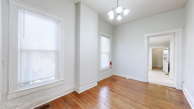 unfurnished room with wood-type flooring, a wealth of natural light, and a notable chandelier