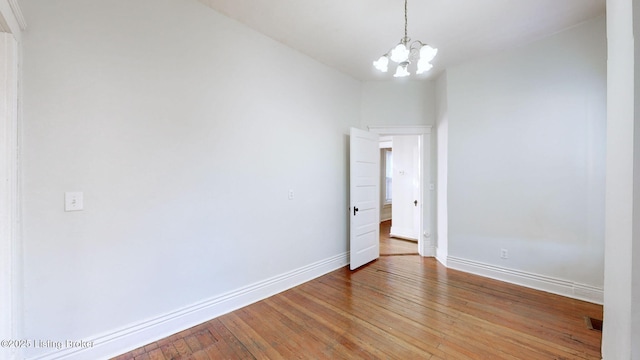 empty room featuring wood-type flooring and a chandelier