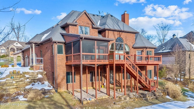 snow covered back of property with a sunroom and a deck