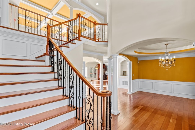 staircase featuring decorative columns, hardwood / wood-style floors, and crown molding