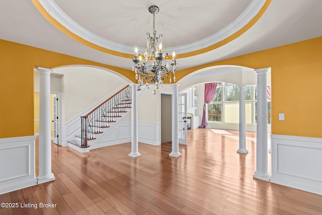 interior space featuring a raised ceiling, ornate columns, and wood-type flooring