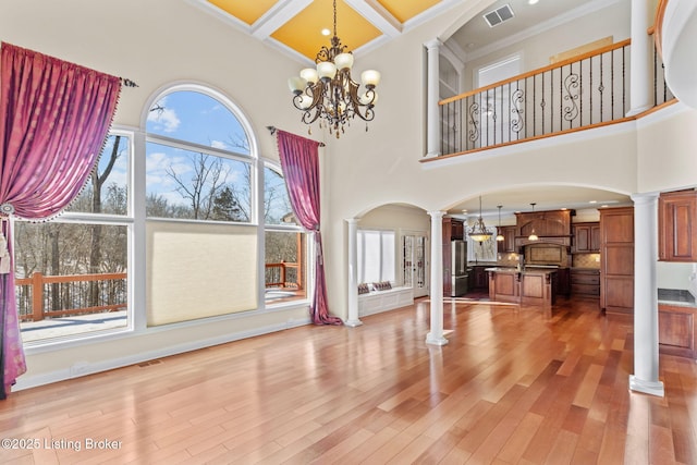 living room featuring coffered ceiling, decorative columns, a towering ceiling, and light wood-type flooring