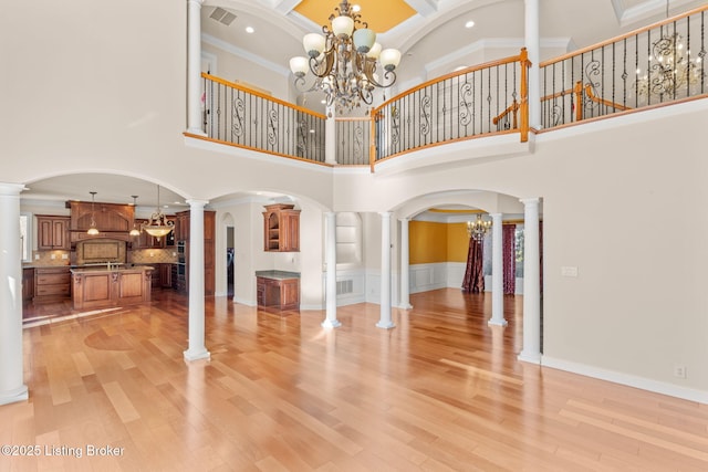 living room featuring a high ceiling, ornamental molding, ornate columns, and an inviting chandelier