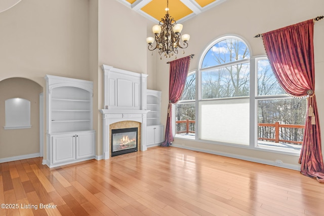 unfurnished living room with a tile fireplace, a towering ceiling, a chandelier, light hardwood / wood-style flooring, and coffered ceiling