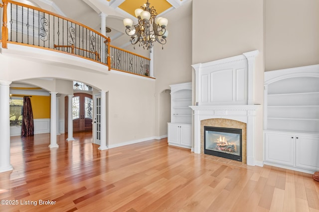 unfurnished living room featuring french doors, a tiled fireplace, a high ceiling, light hardwood / wood-style floors, and decorative columns