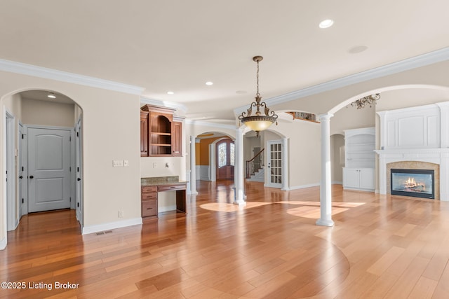 unfurnished living room with light wood-type flooring, crown molding, ornate columns, and a tile fireplace