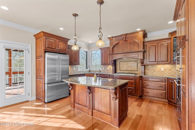 kitchen featuring stainless steel appliances, an island with sink, decorative backsplash, stone countertops, and light wood-type flooring