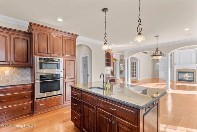 kitchen with hanging light fixtures, sink, tasteful backsplash, a kitchen island with sink, and ornamental molding