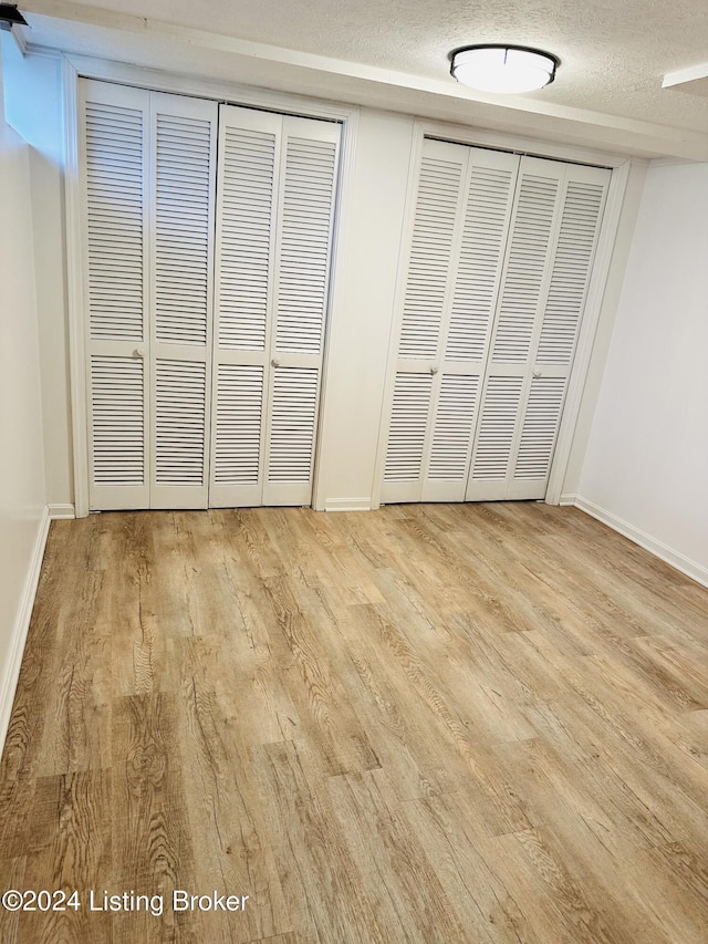 unfurnished bedroom featuring multiple closets, light hardwood / wood-style floors, and a textured ceiling