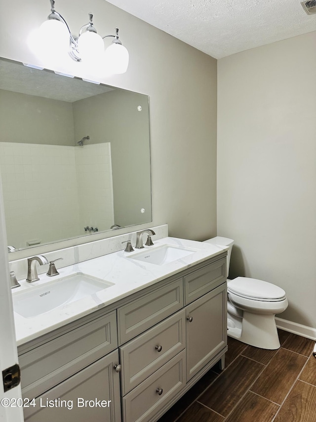 bathroom with toilet, a textured ceiling, walk in shower, and vanity