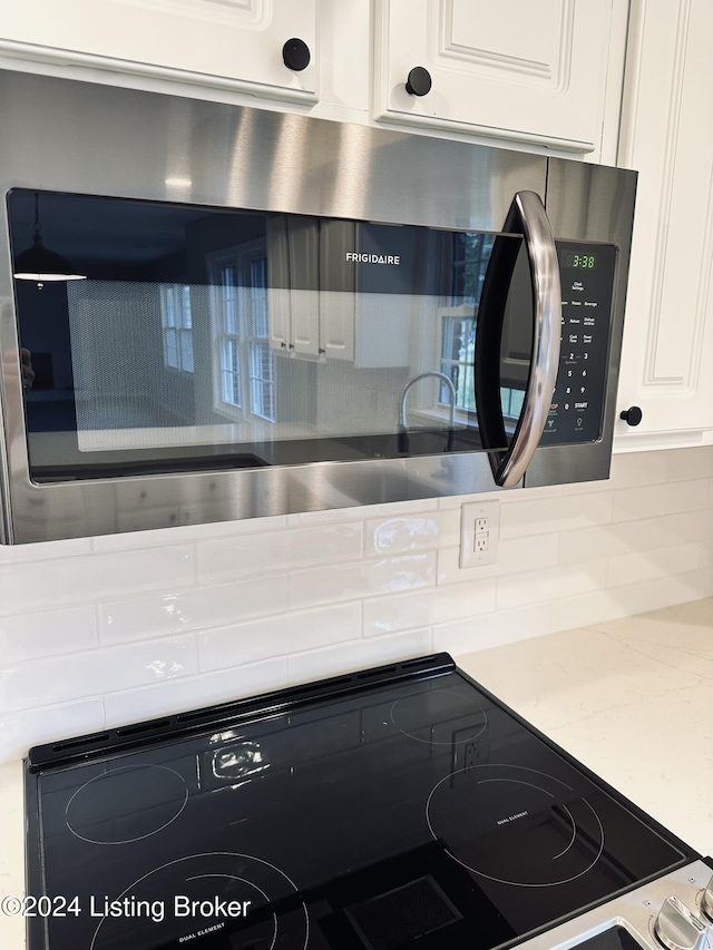 interior details featuring backsplash, white cabinetry, and appliances with stainless steel finishes