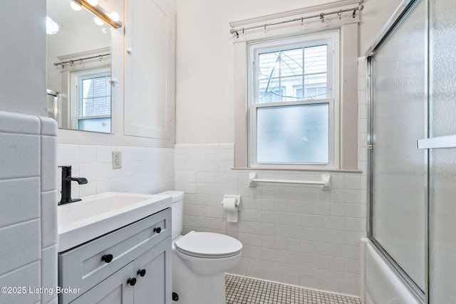 full bathroom featuring toilet, bath / shower combo with glass door, tile walls, tile patterned flooring, and vanity