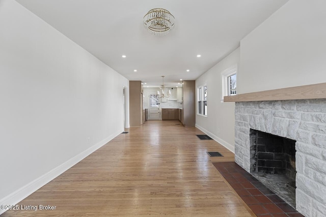 unfurnished living room featuring hardwood / wood-style floors, an inviting chandelier, and a stone fireplace