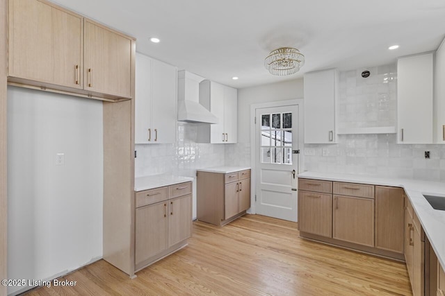 kitchen with light brown cabinets, backsplash, light hardwood / wood-style flooring, and wall chimney range hood