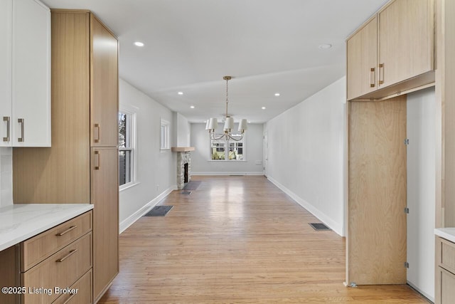 interior space with light stone counters, light hardwood / wood-style floors, hanging light fixtures, and light brown cabinets